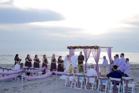 Purple Beach Wedding Ceremony with Floral Accents and Draped Aisle Decorations