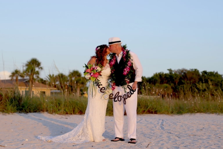 Newlywed Couple Holding Floral We Eloped Banner After Beach Elopement Ceremony