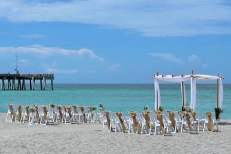 Florida Beach Wedding Ceremony Set with white chairs tied with burlap sashes and a 4-post white-draped Chuppah arbor in Venice, Florida