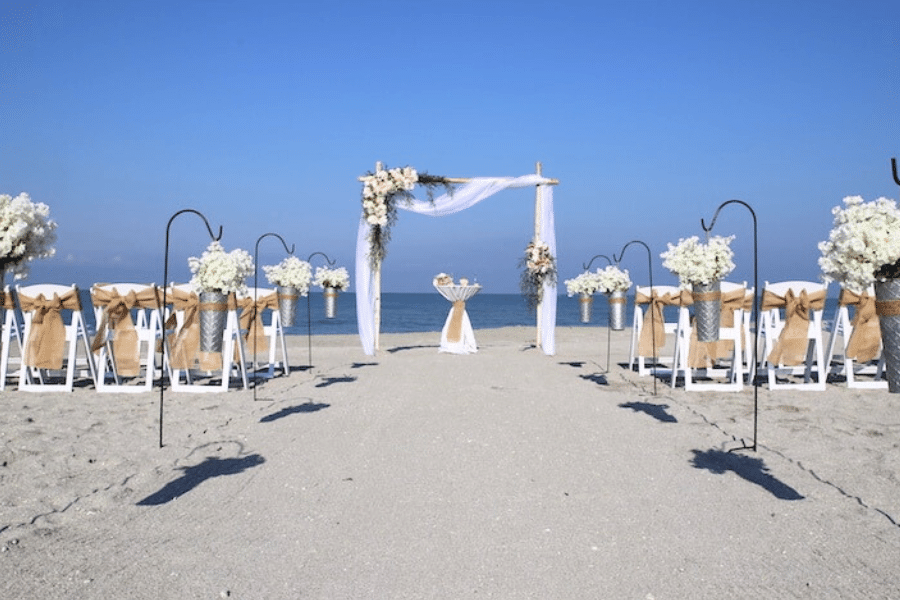 Beach Wedding Ceremony setup on Florida beach with blue skies. The arch is draped with white organza and asymmetrical flower arrangements.