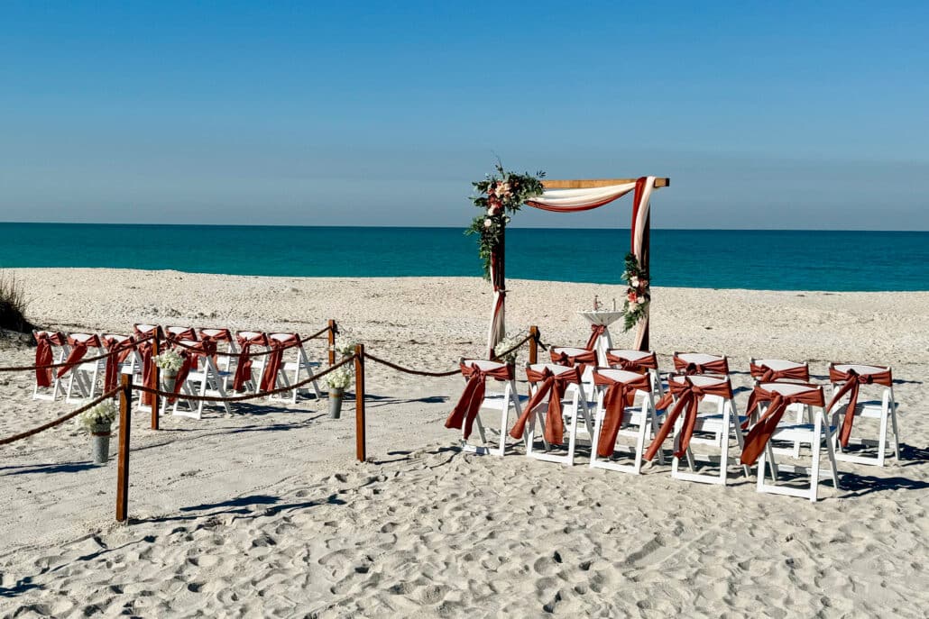 Romantic beach wedding ceremony design, multi-color drapery in shades of rust/terra cotta. wedding arch backdrop with wood frame for Florida beach wedding | best wedding locations in Florida