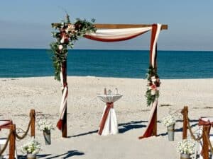 Romantic beach wedding ceremony design, multi-color drapery in shades of rust/terra cotta. wedding arch backdrop with wood frame for Florida beach wedding