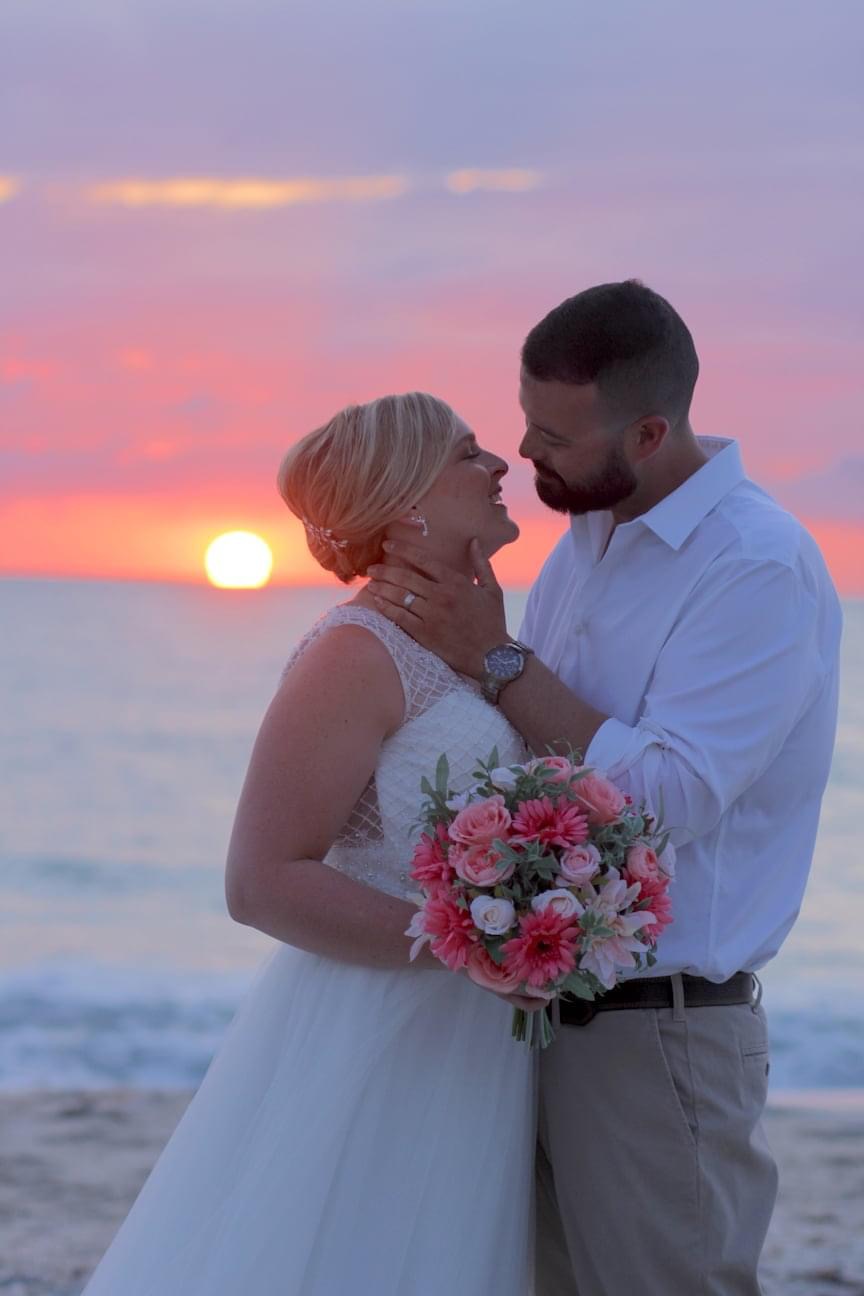 Bride and Groom stand on the beach shore during a pink sunset beach wedding
