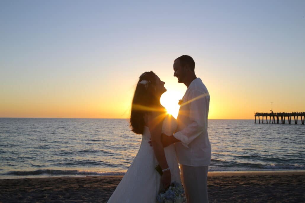 bride and groom newlyweds embrace with the setting sun behind them, and rays showing between them